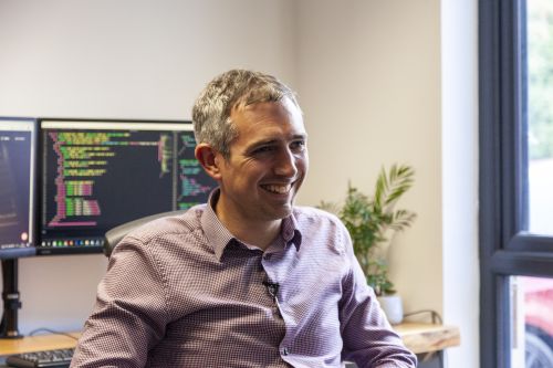 Award-Winning Digital Agency founder smiling with computers showing code behind him