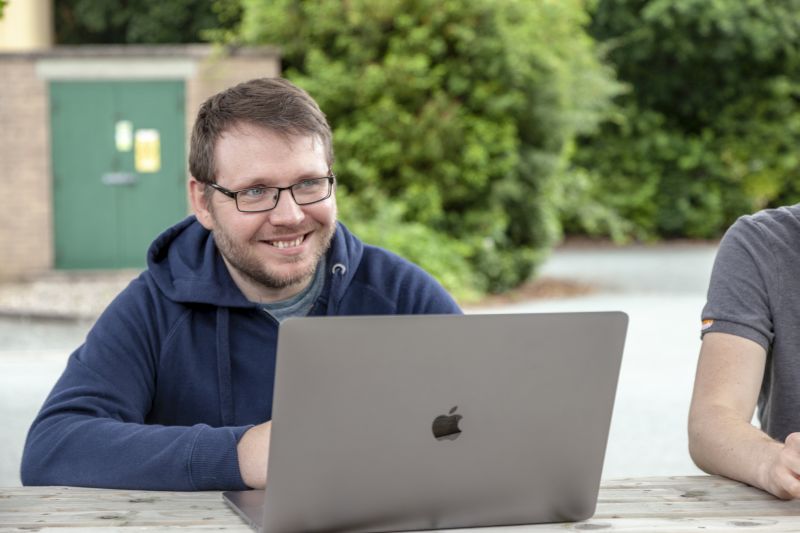 Web developer sitting outside smiling and using a laptop