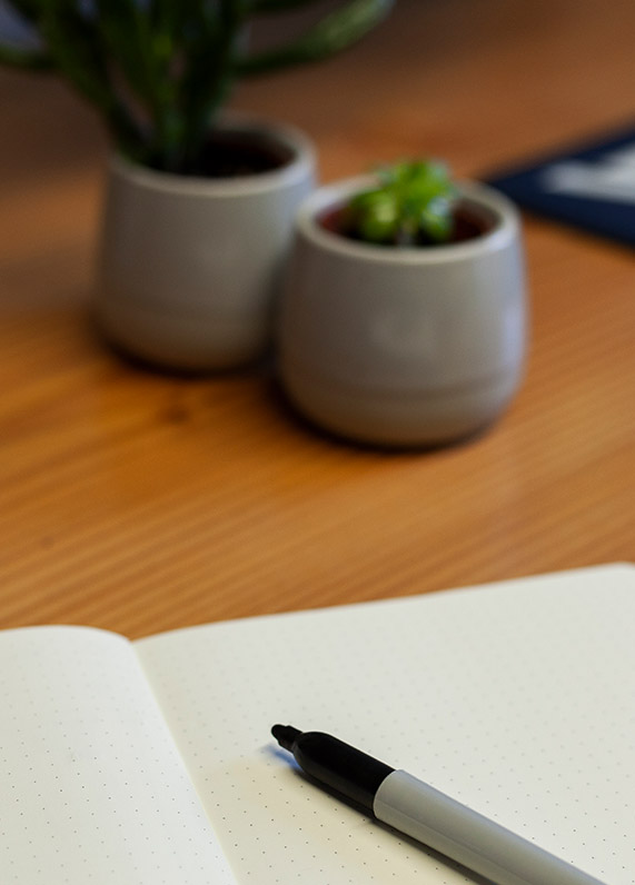 An empty note pad on a wooden desk with small plant pots in the background