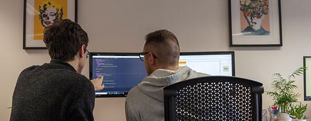 Two SuperControl developers working at a desk with one pointing at the screen