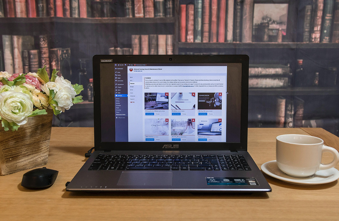 A laptop on a desk with flowers and a mug, the laptop is showing the wordpress editing area