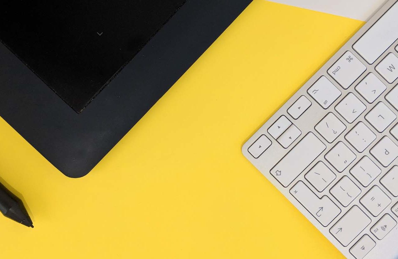 Apple keyboard with a black tablet & stylus on a yellow surface