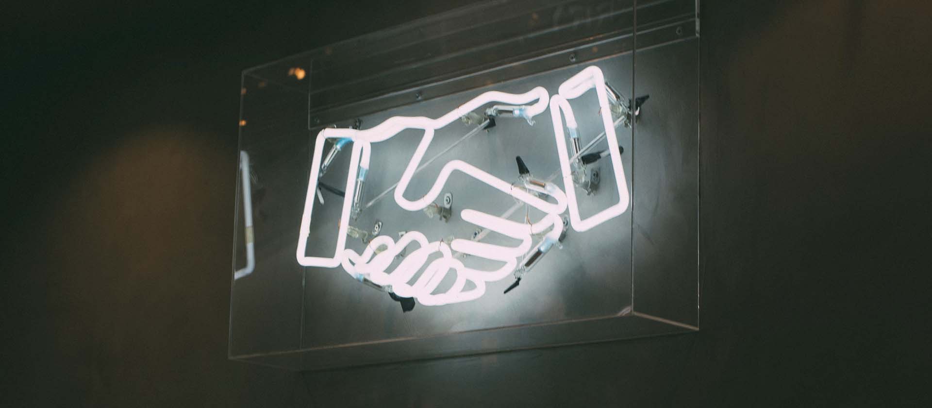 A LED white lit partnership handshake in a clear casing on a grey wall