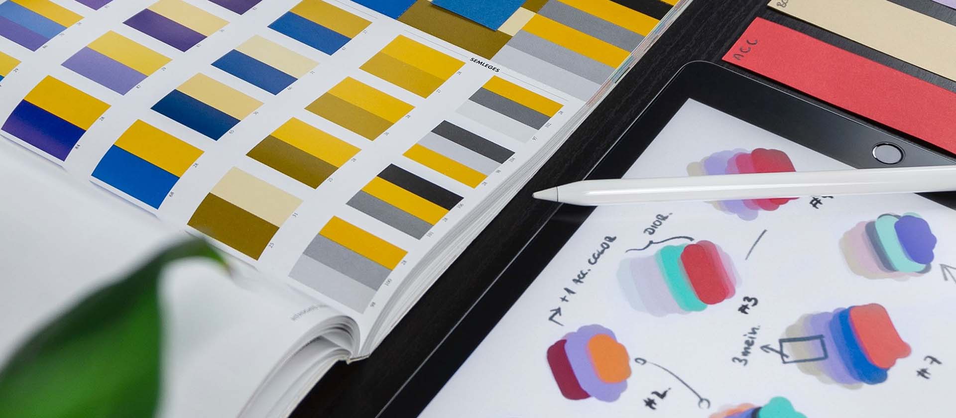 An ipad showing colour testing and a book of colour patterns abobe it, testing for website redesign