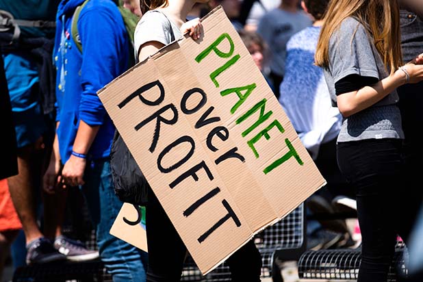 A group of sustainable development protestors, one is holding a carboard sign saying 'planet over profit' 