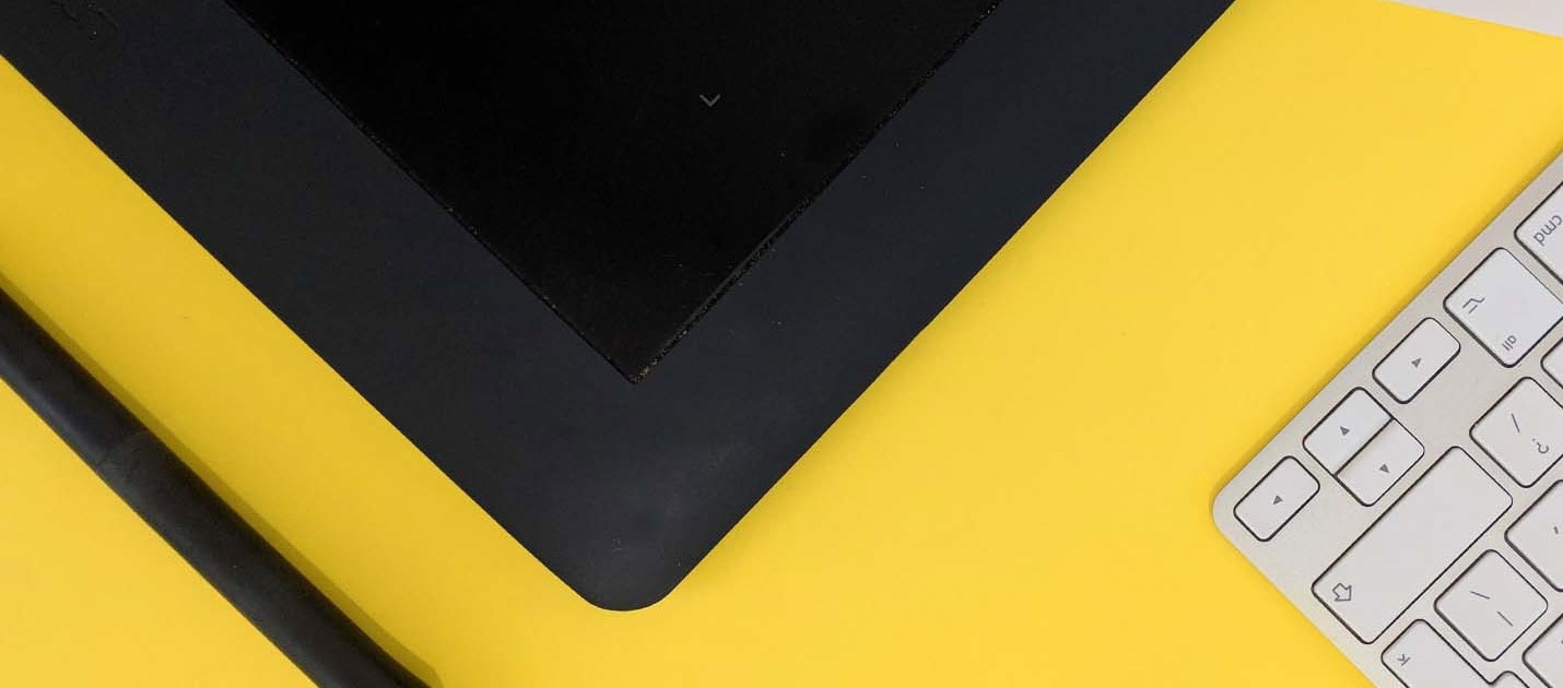 Apple keyboard with a black tablet & stylus on a yellow surface