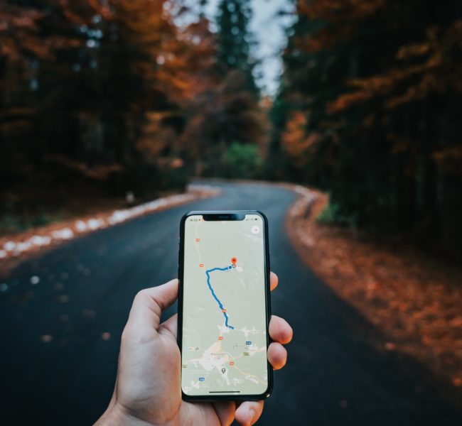Google maps on a phone in someones hand in front of a autumnal road