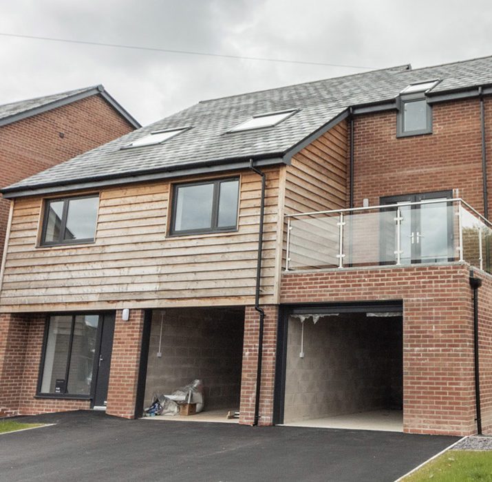 Half brick, half wooden house with two open garage doors and a balcony for Montgomeryshire Homes